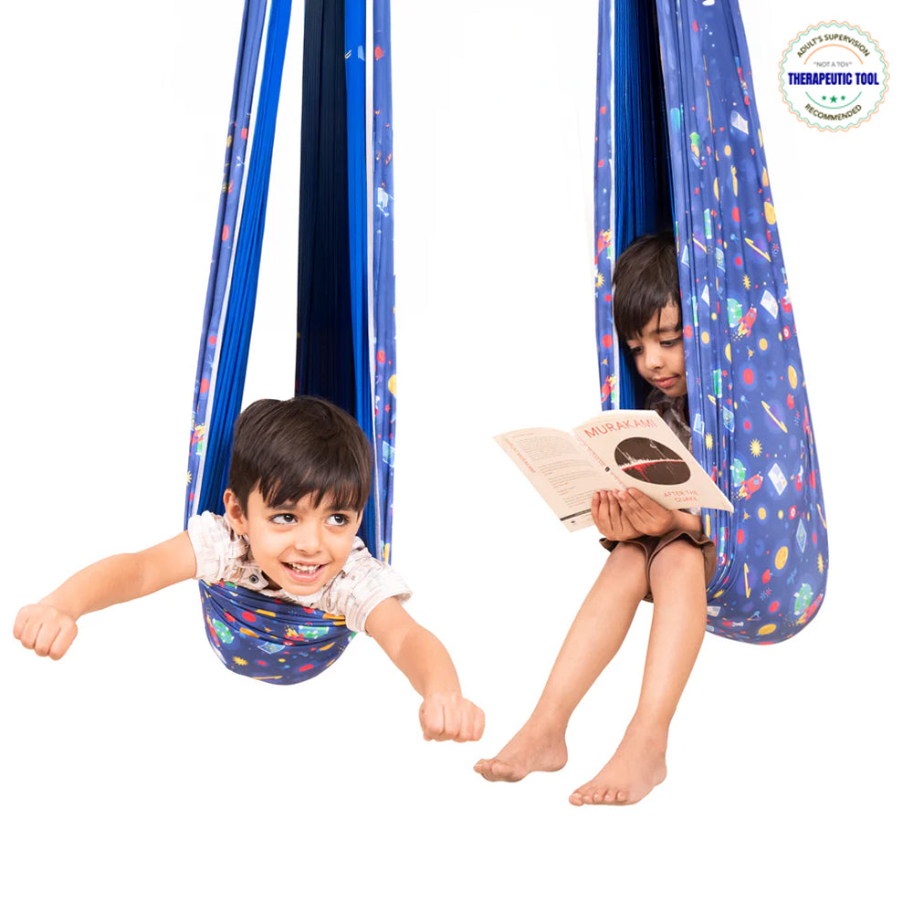 Two children using a blue patterned lycra sensory swing for kids one reading and one pretending to fly