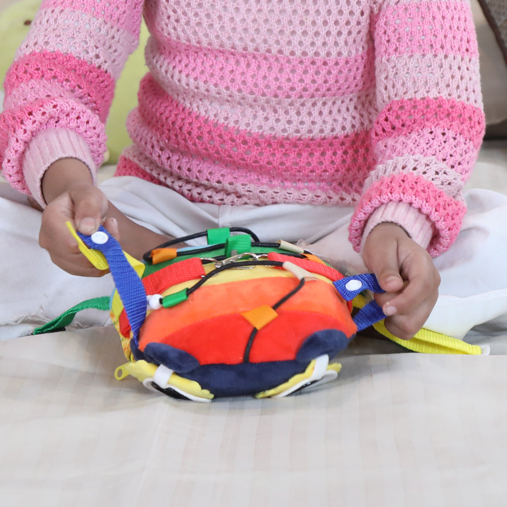 Child holding buckle activity toy for fine motor skills plush turtle with colorful straps and snaps