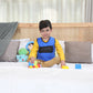 Ableys blue weighted vest for kids worn by smiling boy sitting on bed playing with toy blocks