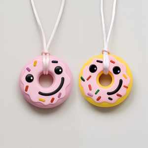 Two donut silicone chewable necklaces for sensory needs by Ableys in pink and yellow with smiling faces