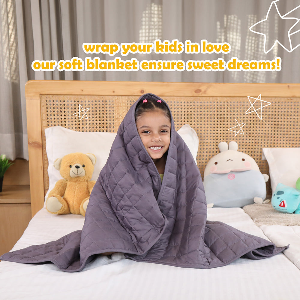 Ableys weighted blanket for kids gray quilted blanket wrapped around smiling girl on bed with plush toys