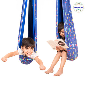 Two children using a blue patterned lycra sensory swing for kids one reading and one pretending to fly