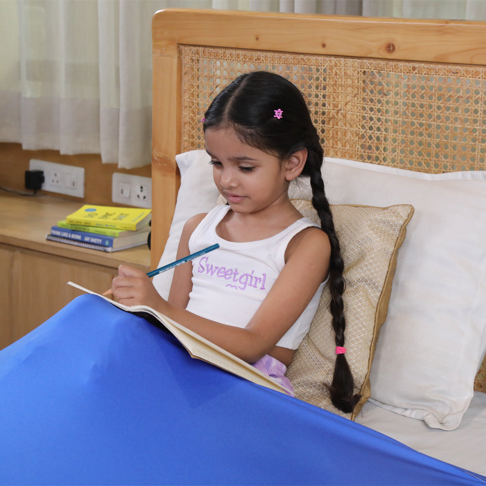 Young girl sitting in bed writing with a blue compression bed sheet for sensory needs covering legs