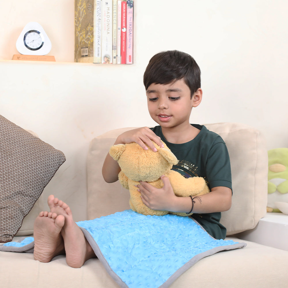 Ableys blue plush weighted lap pad for focus on a child sitting on couch holding a teddy for calming